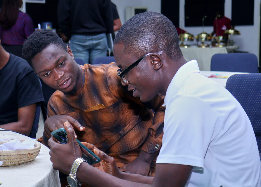 Two male ALX learners discussing what they see on the screen of a mobile phone