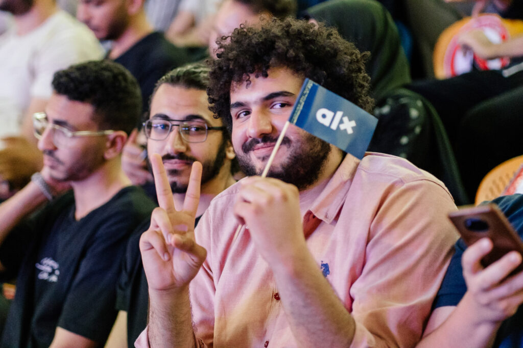 ALX learner at the Karibu ceremony in Cairo holding up an ALX flag and a peace sign