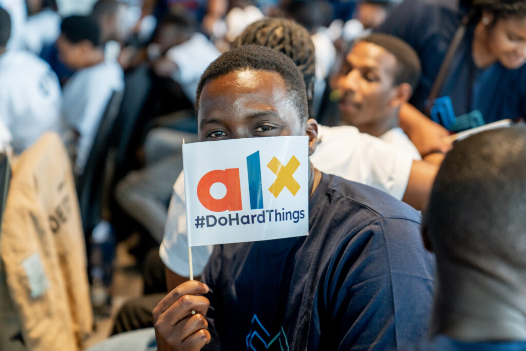 ALX learner holding an ALX #DoHardThings glag across his face at the Karibu ceremony in Kigali