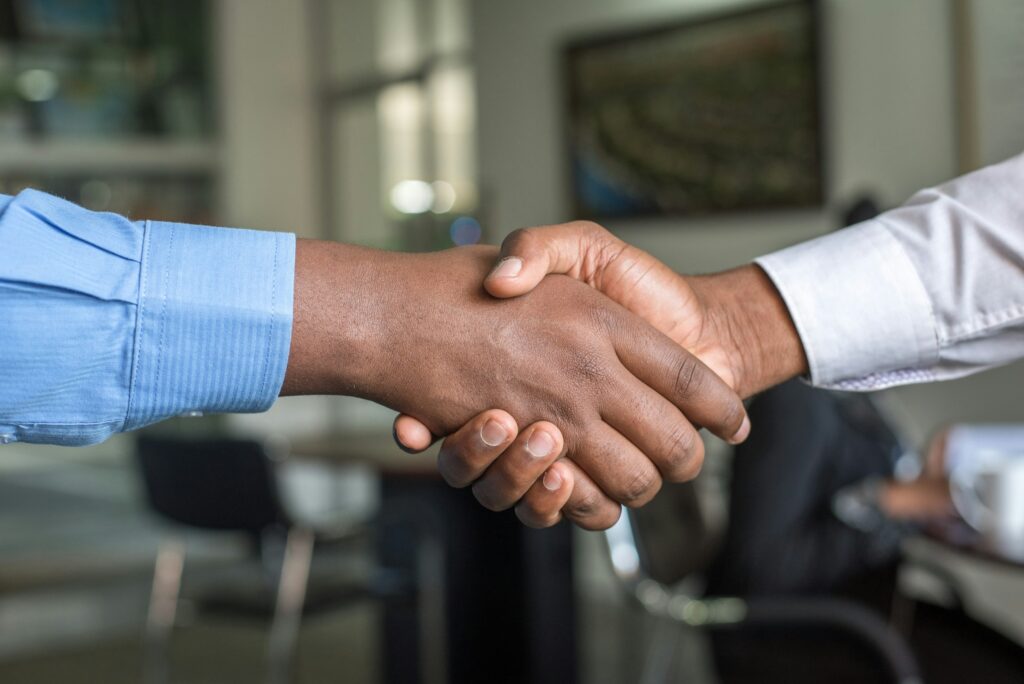 Two people shaking hands, one with a blue long sleeve shirt, one with a white long sleeve shirt.