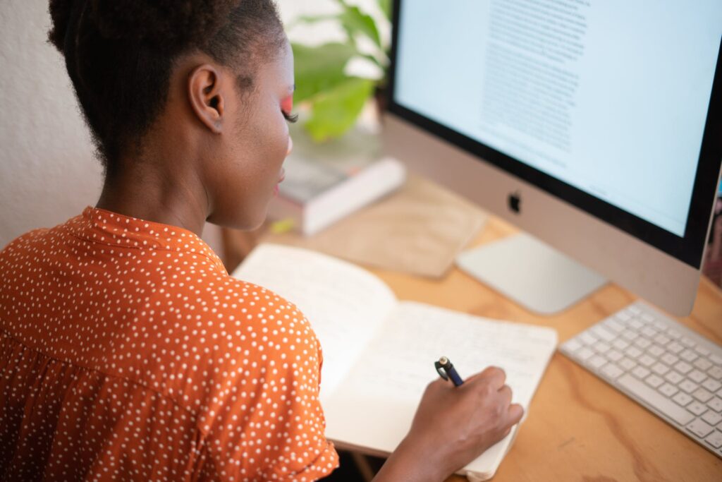 Woman sitting at her desk in front of a computer screen writing in a notebook