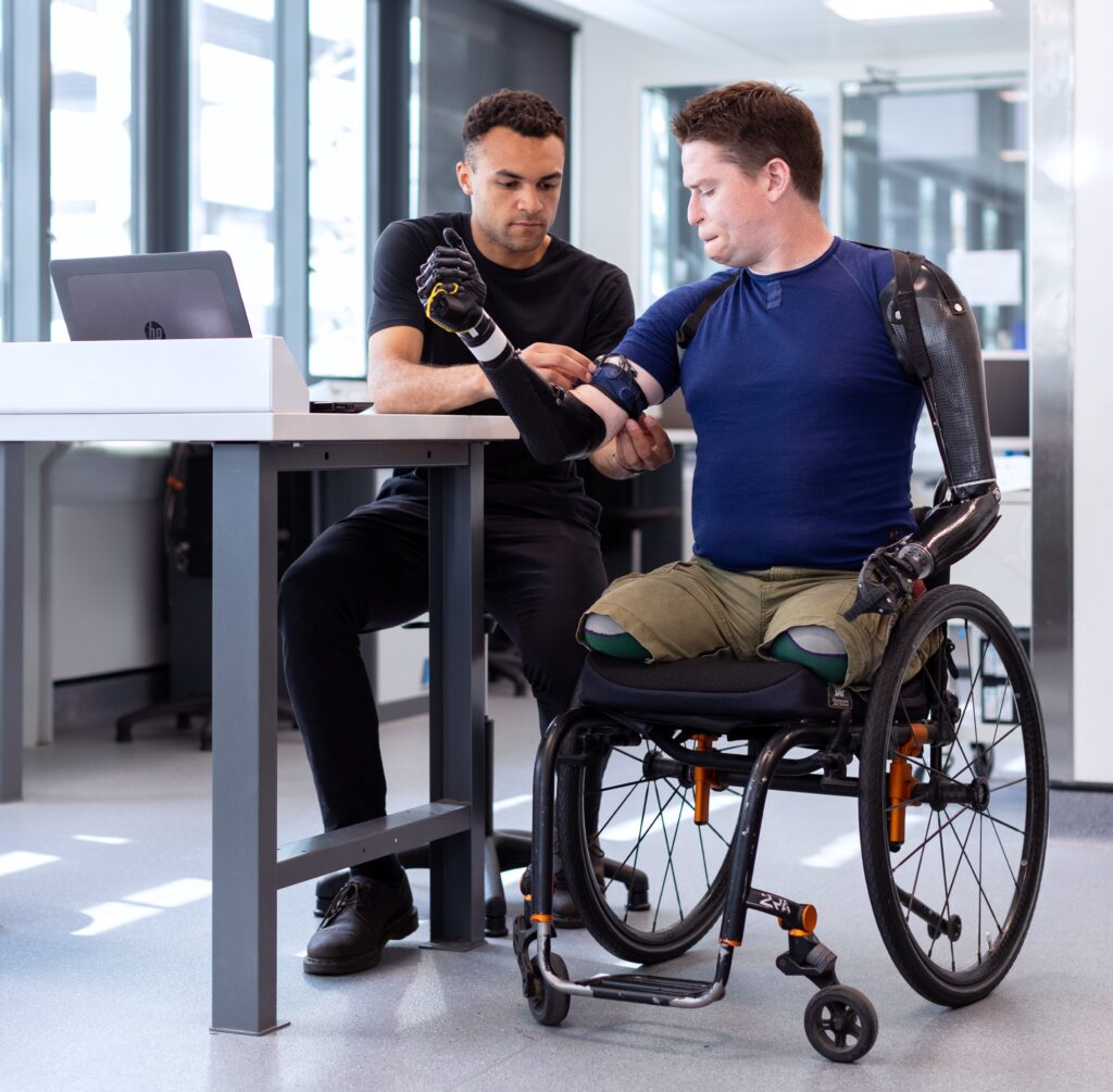 Engineer fitting a prosthetic arm on a man in a wheelchair