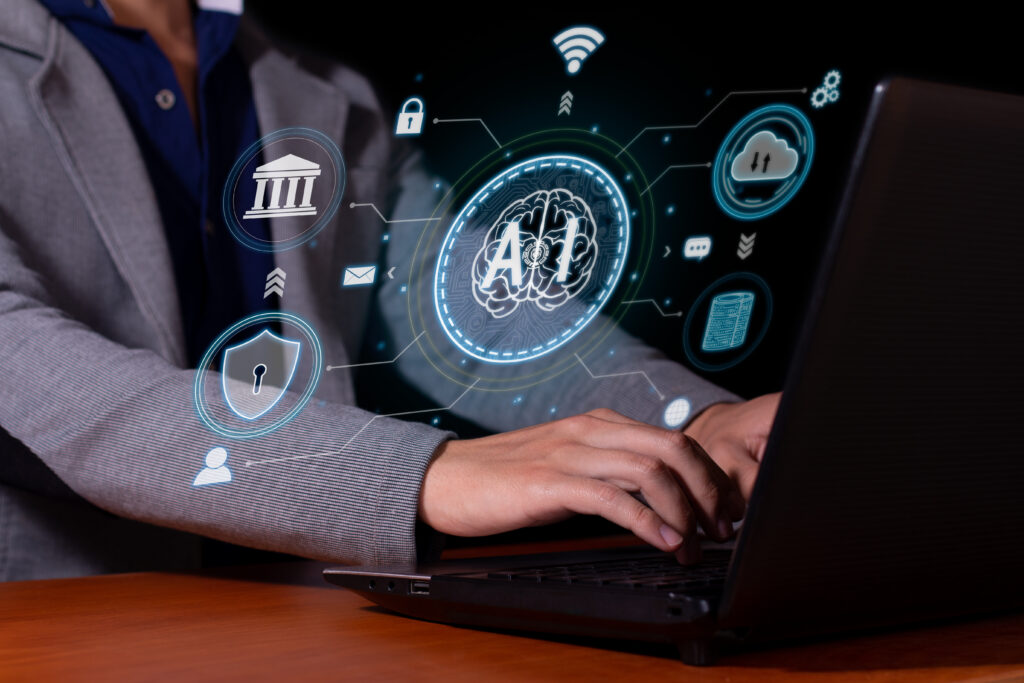 A man sitting in front of a laptop with his hands above his keyboard. Hovering above his hands is the word "AI" with icons and other imagery that seems to suggest uploading data to the cloud, security, banking, and wifi.