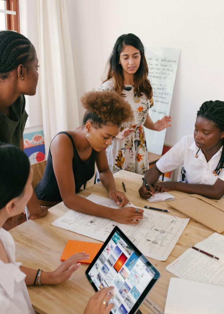 Photo of women sitting around a stack of papers as if at a meeting.