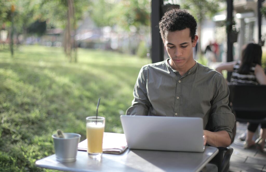 A man sitting behind his computer outside at a cafe working on university assignments