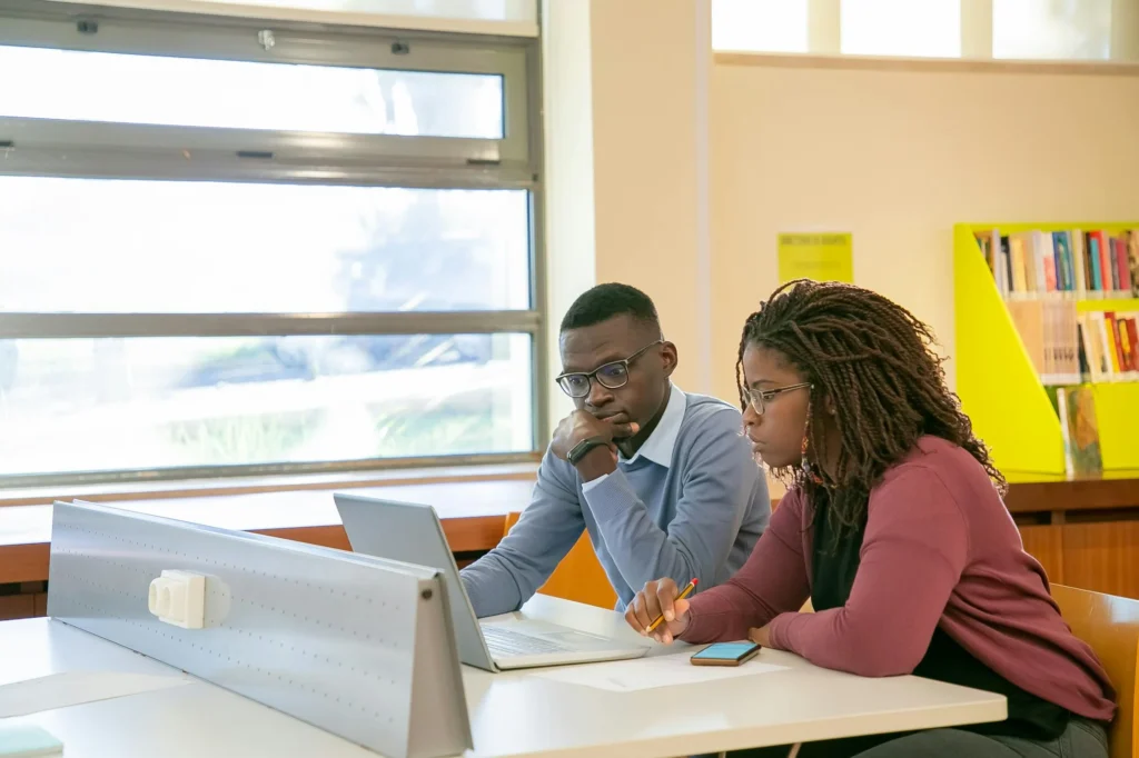 Two people working together behind a computer, studying online.
